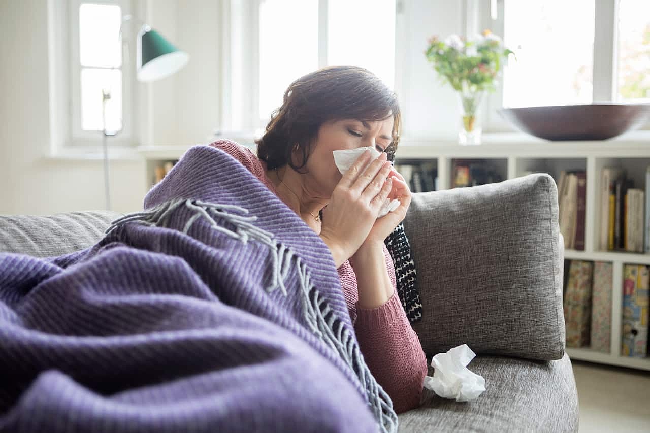 A woman lies on a sofa blowing her nose