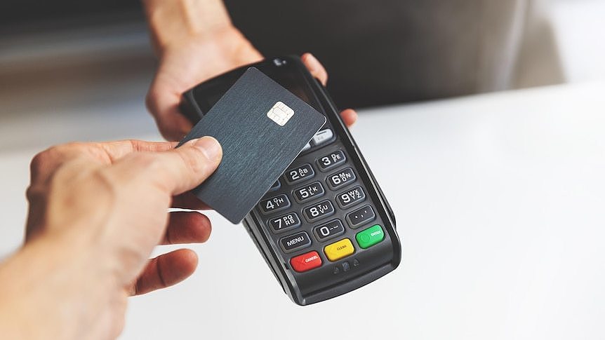 A person taps a black credit or debit card on a payment terminal.