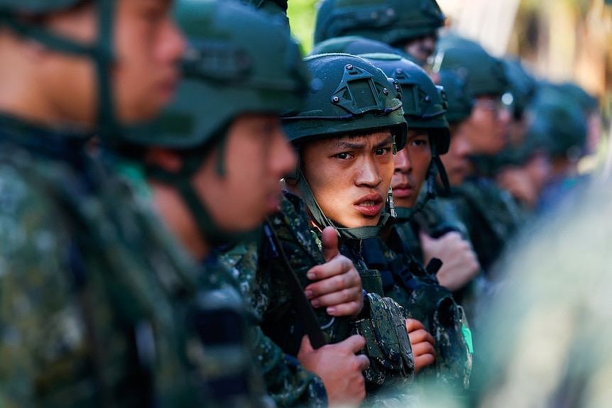 A young male soldier wearing combat uniform standing with fellow soldiers