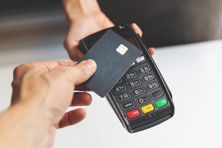 A person taps a black credit or debit card on a payment terminal.