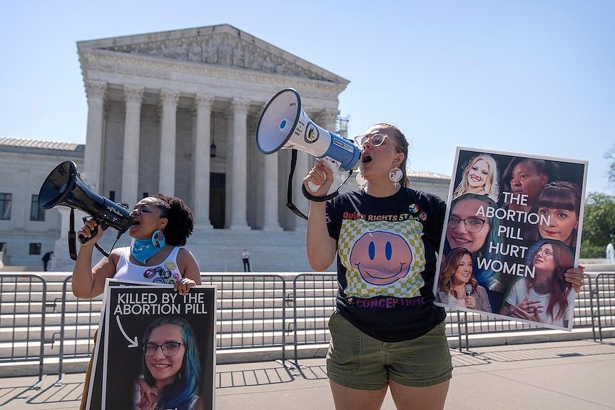 Two women with megaphone stand in front of a court house holding a protest against abortion