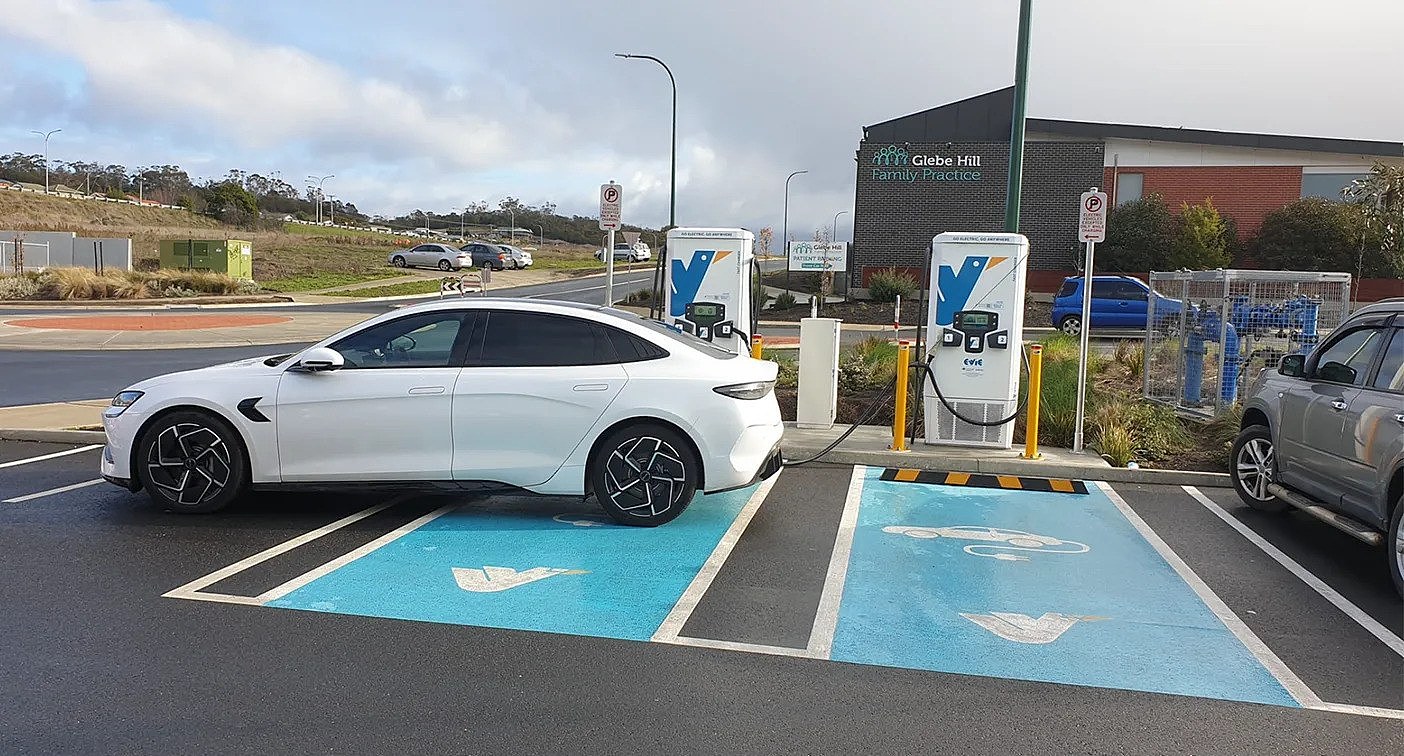 An electric vehicle motorist is seen using a charger at one station, parking over another, and two separate motorcycle bays in Tasmania. 