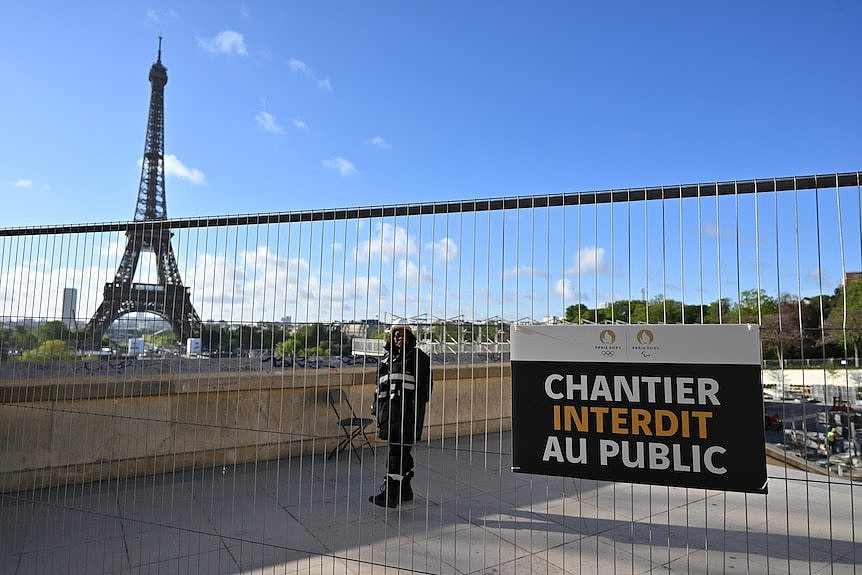 A security guard stands near a fence, with the Eiffel Tower in the background