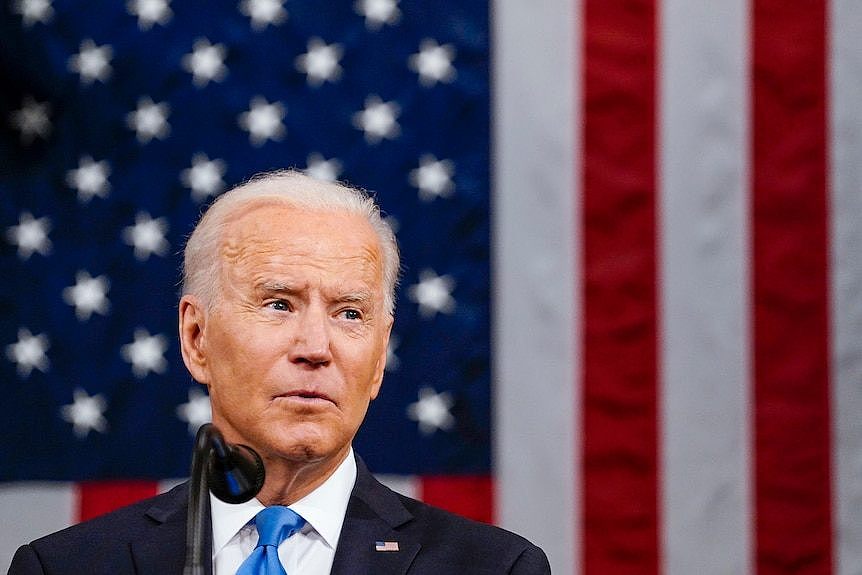 Joe Biden speaking into a microphone in front of an American flag