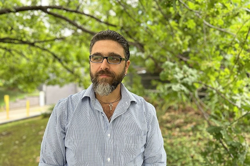 A man with dark hair and glasses in a checked shirt.