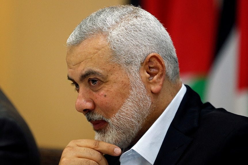 Ismail Haniyeh puts his right index finger across his stubbled chin as he tilts his head down slightly and looks forwards.