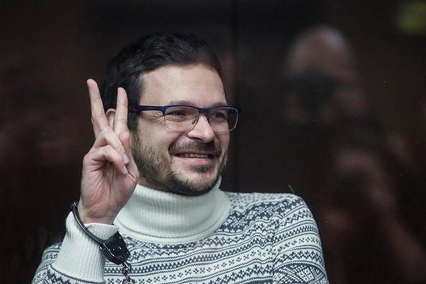 Ilya Yashin gestures with two fingers in peace sign while handcuffed inside a glass cage in a Moscow court.