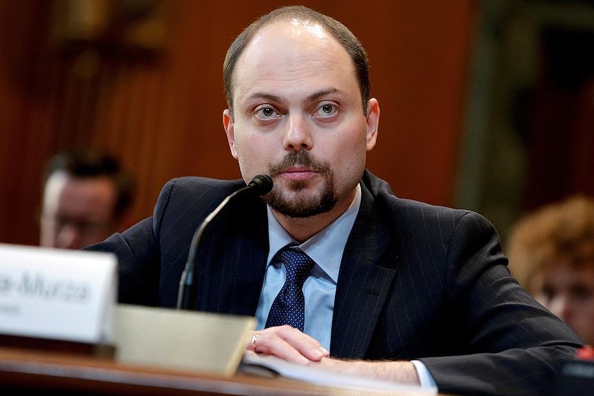 A man sits at a table in front of a microphone.