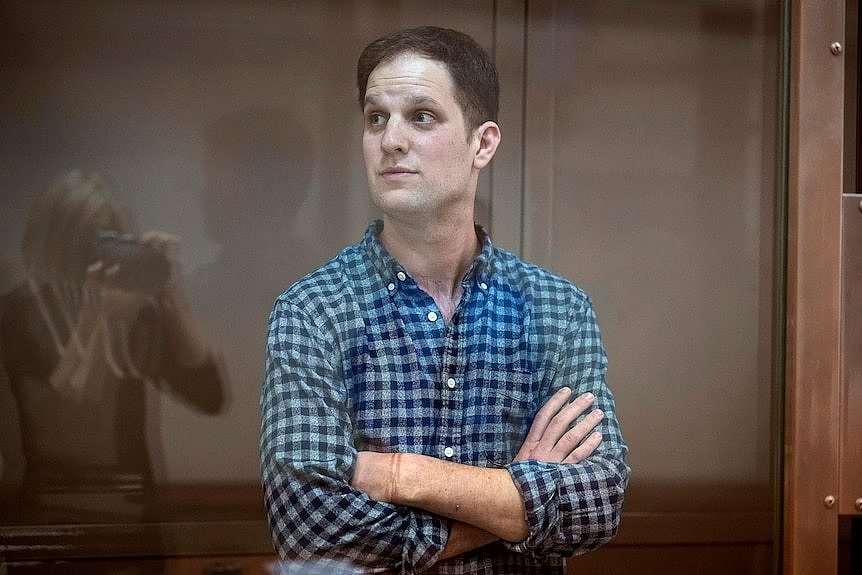 A man stands behind a pane of glass with his arms crossed.