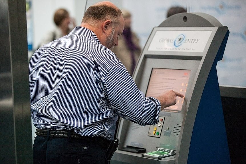 A man stands at a touchscreen which has a 'Global Entry' sign above it.