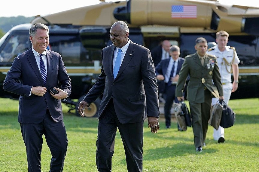 Richard Marles and Lloyd J Austin smile at each other in front of a military helicopter. 