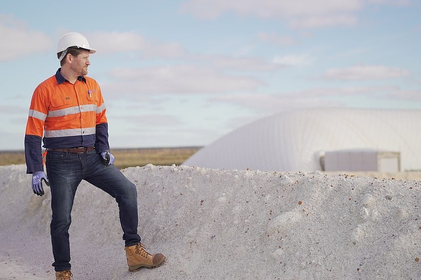 A man standing on rocky ledge looking at a large white building. 