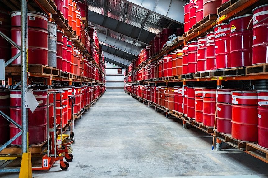 An aisle full of large red drums on shelves. 