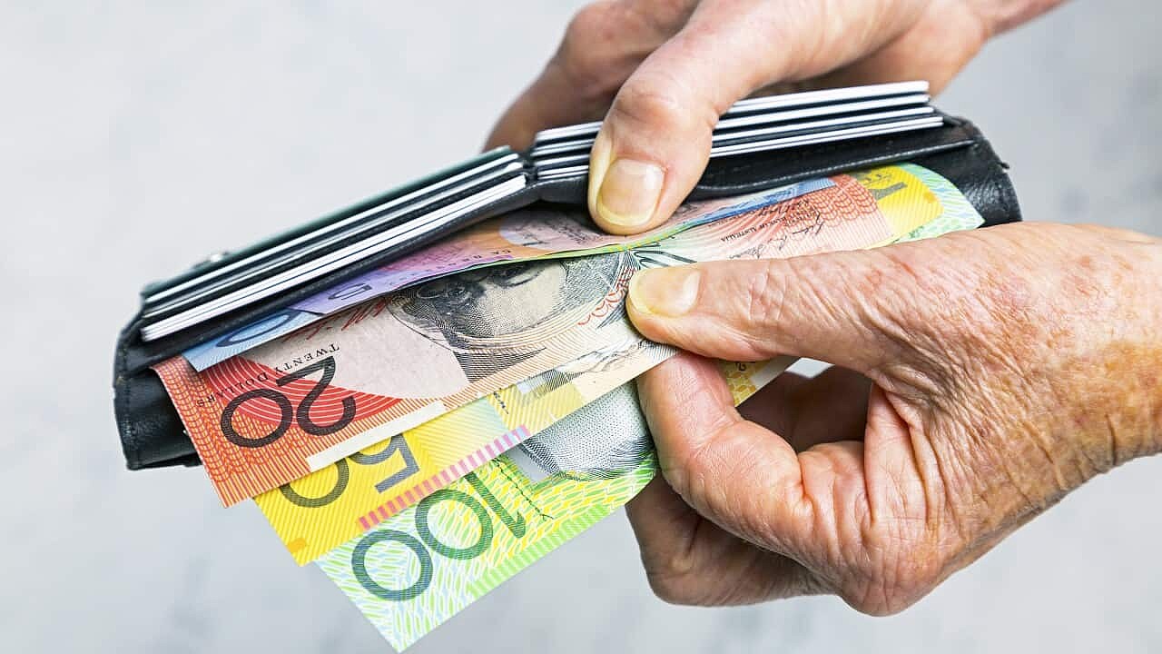 A close-up photo shows two hands taking Australian banknotes out of a purse. 