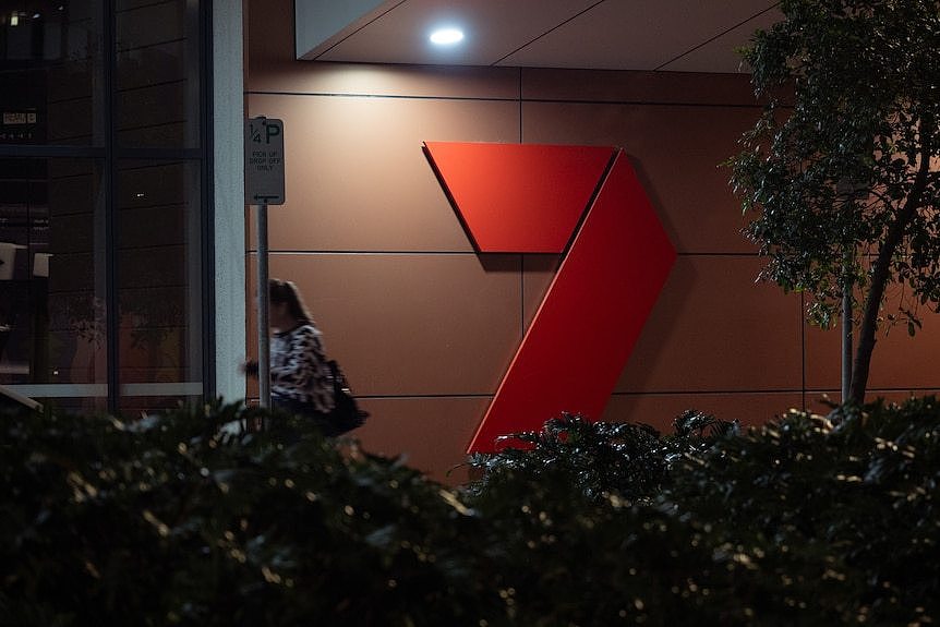 A person walks past a large 7 logo, it is lit from above by a spotlight.