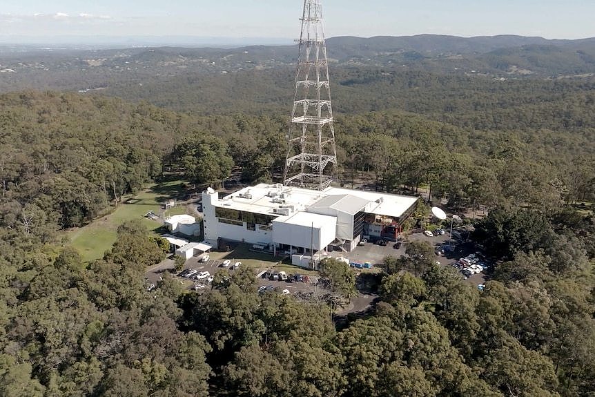 A building surrounded by dense bushland. It has a large television broadcast tower on top of it.