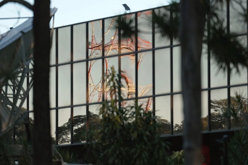 A low level building with reflective glass. Reflected in the glass is a television broadcast tower.