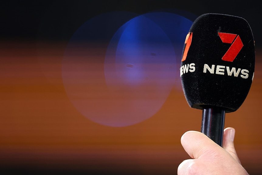 A hand holding a microphone. Foam on top of the microphone has '7 News' on it.