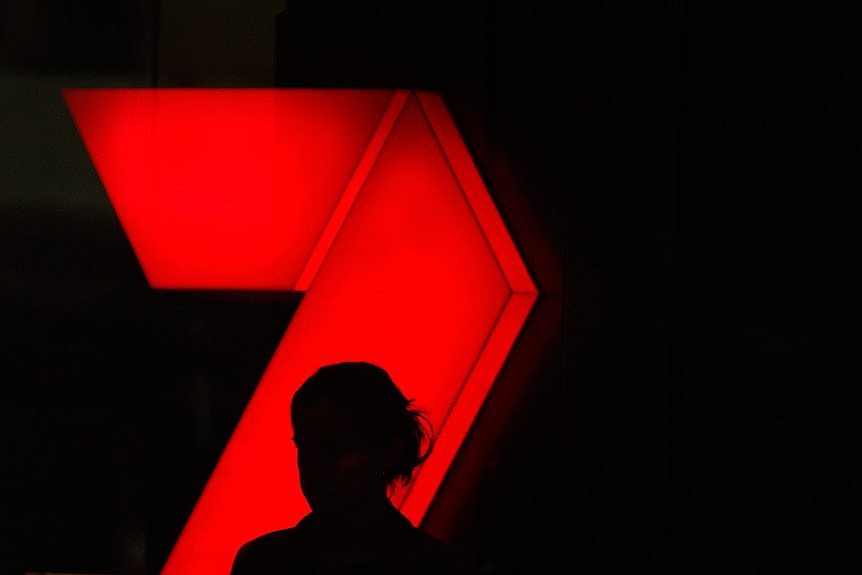 A person is silhouetted against a large illuminated red channel 7 logo.