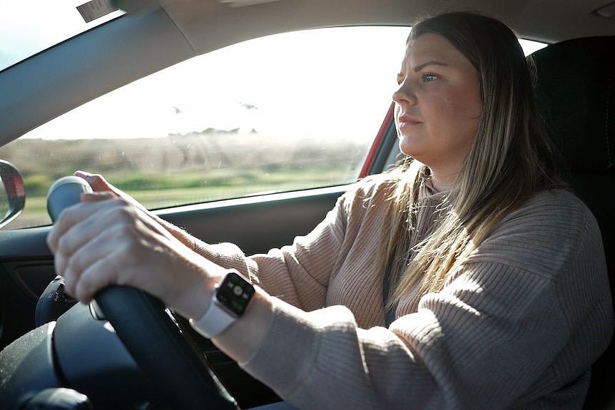 A photo taken from a passenger seat of a woman driving a car. She is looking ahead.