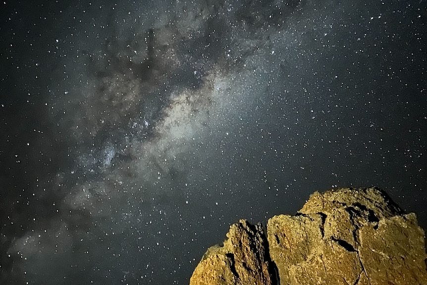 A beautiful photo of the night sky with a lit up rock in the foreground. 