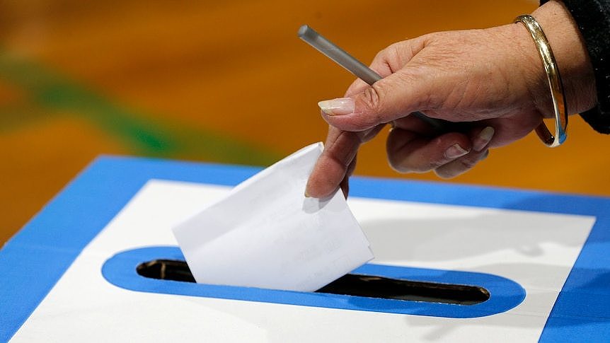 a woman putting a voting ballot paper in a box