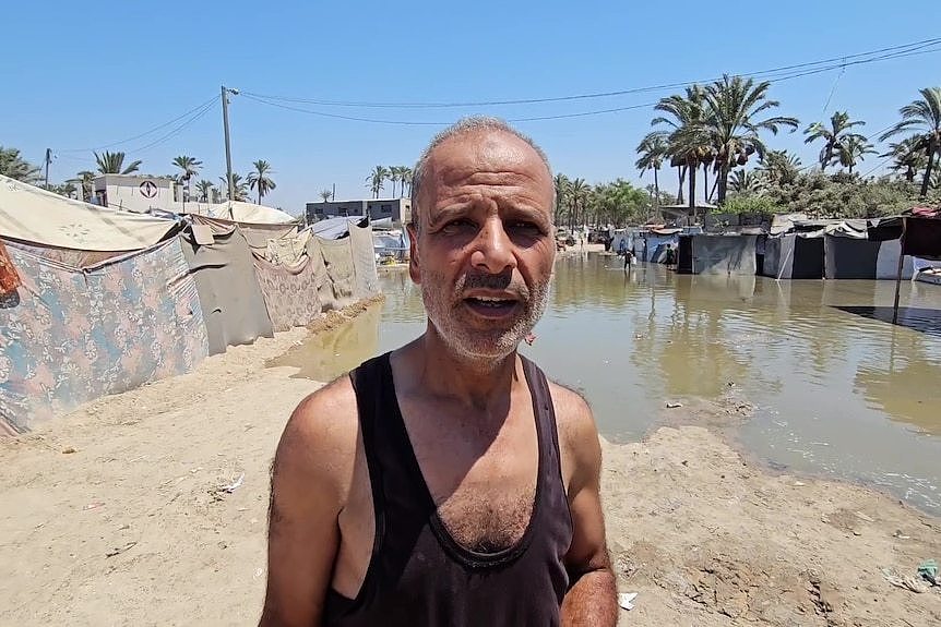 A man wearing a singlet standing on dirt with a part covered in green brown dirty water