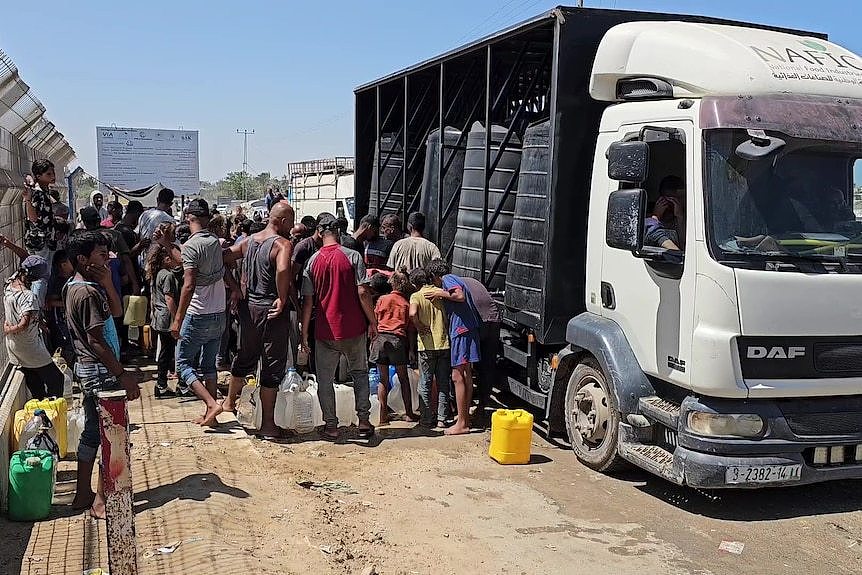 People carrying buckets lining up at a truck to fill water