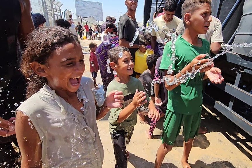 Kids being splashed by water from a hose next to a truck