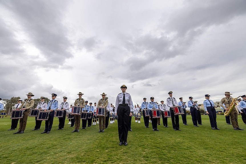 Rows of people in military uniform stand in a field.