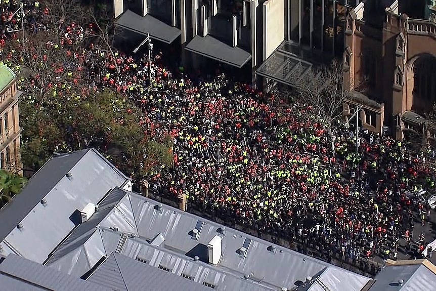 An aerial shot of people wearing hi vis standing along a street.