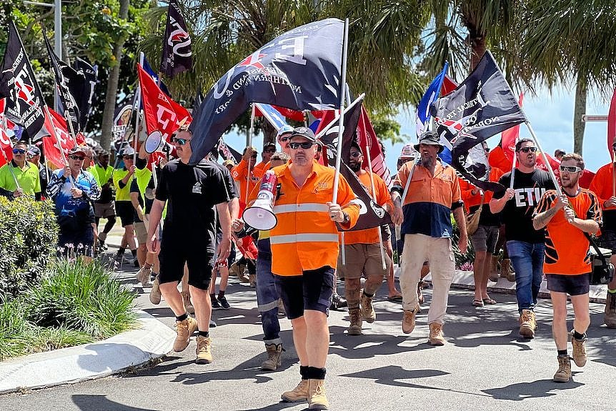 Rob Hill holds a megaphone and a flag and leads a crowd of hundreds down a street.