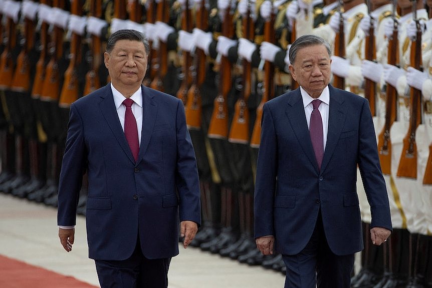 Xi Jinping and To Lam walk side by side in front of a lineup of uniformed soldiers. 