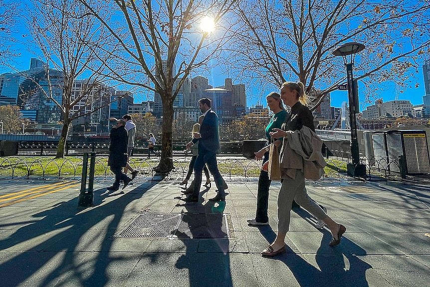 A group of pedestrians walking along a footpath by the Yarra River on a sunny day.