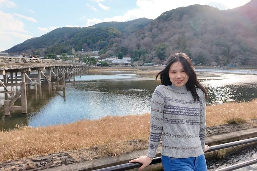 Woman with long hair leaning against the fence smiling to camera.