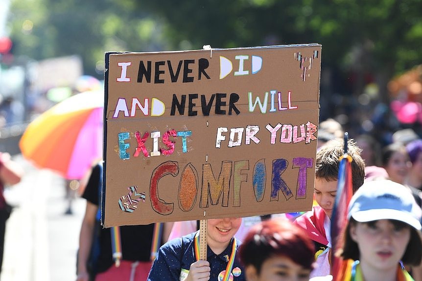 A rallygoer holds up a bright sign that says 'I never did and never will exist for your comfort'