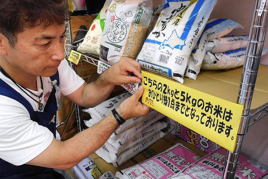 A supermarket worker putting up a sign in Japanese on a rice shelf. 