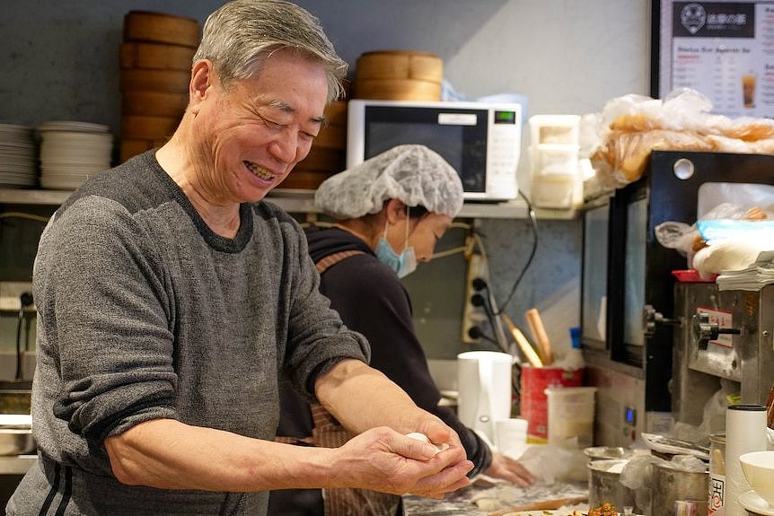 an older man handles dumplings in a kitchen's preparation area