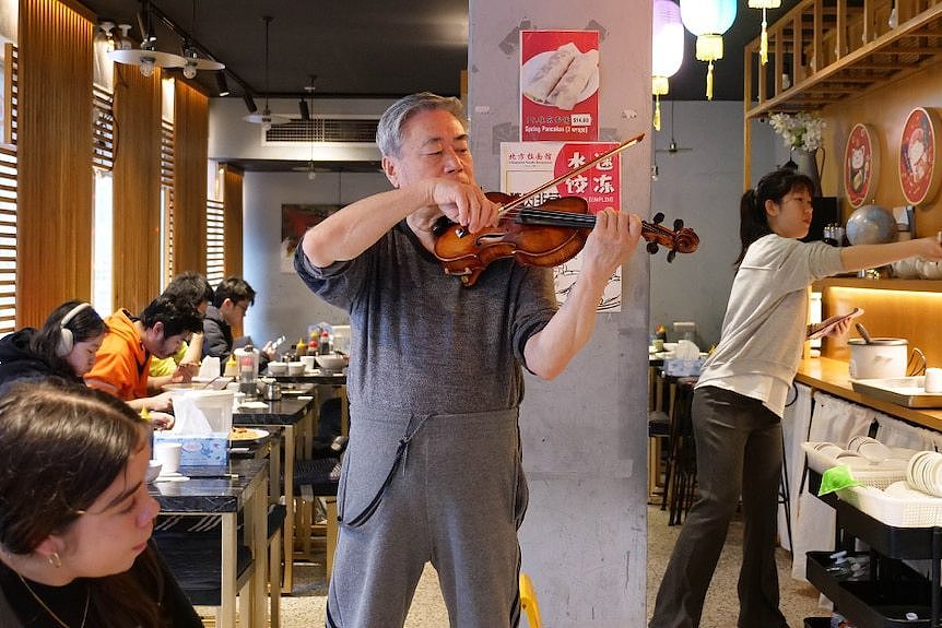 a man stands in the middle of a busy Chinese restaurant plays a violin