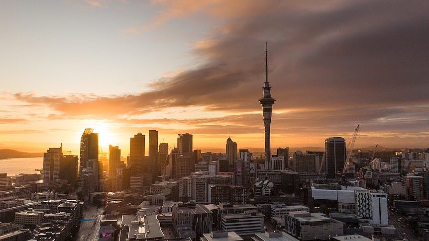 An orange sun sets over a city skyline, casting orange light across the horizon