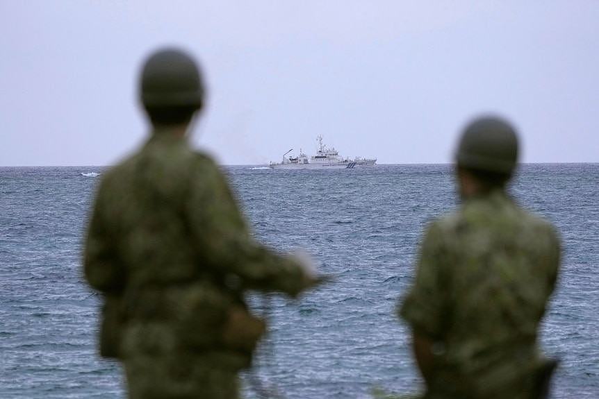 Japanese military members watch a coast guard ship searching for a missing helicopter at sea