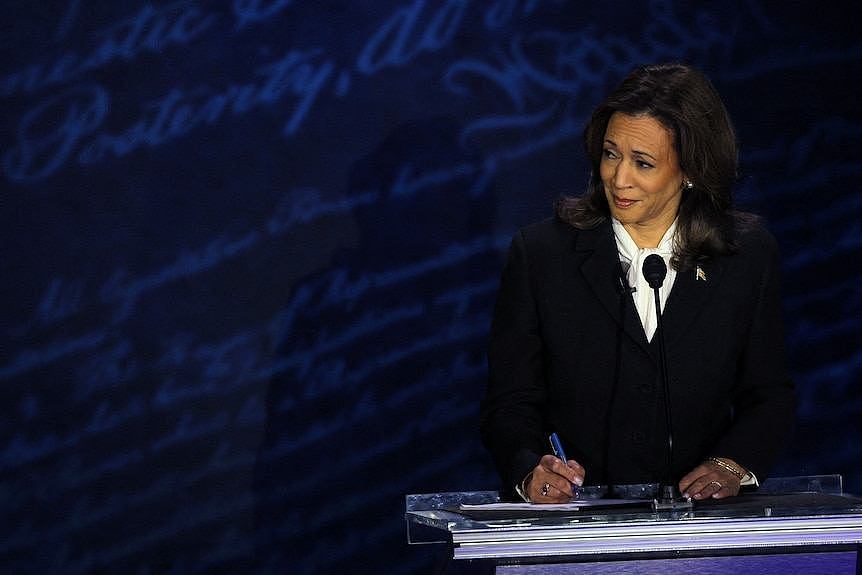 Kamala Harris stands at a debate podium and takes notes.