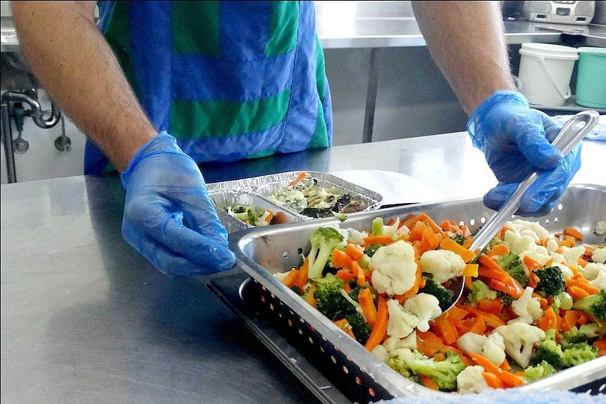 Gloved hands preparing a tray of vegetables.