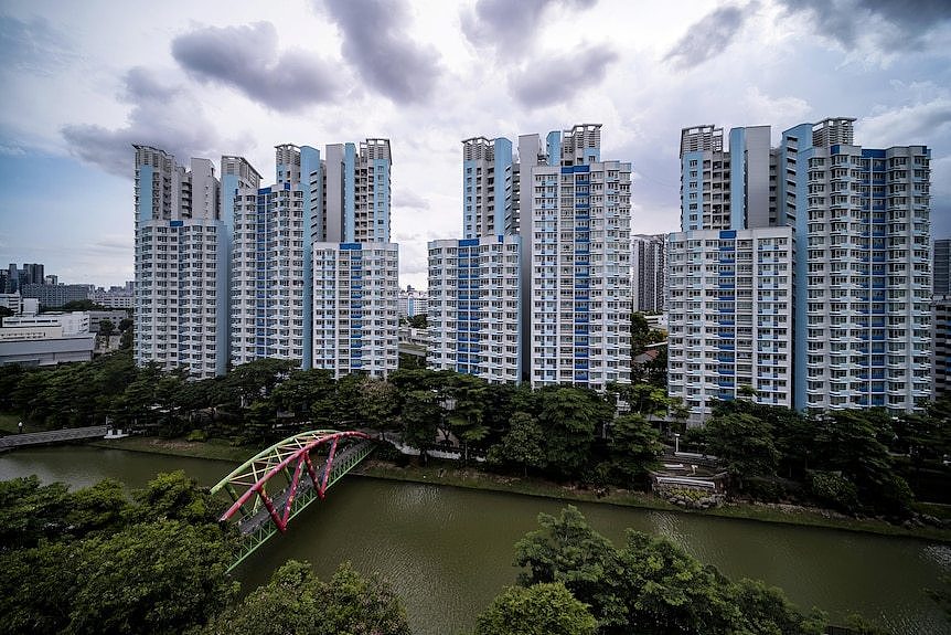 An aerial view o a bridge over a river lined with trees, as high rises stand in the background. 