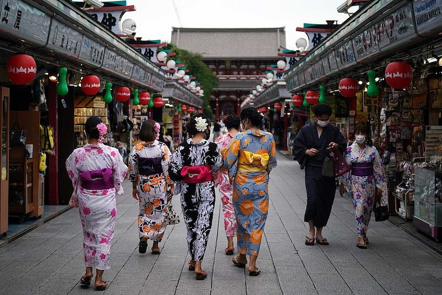 A group of women in Japanese traditional wear walk past two women in face masks in an ornate temple.