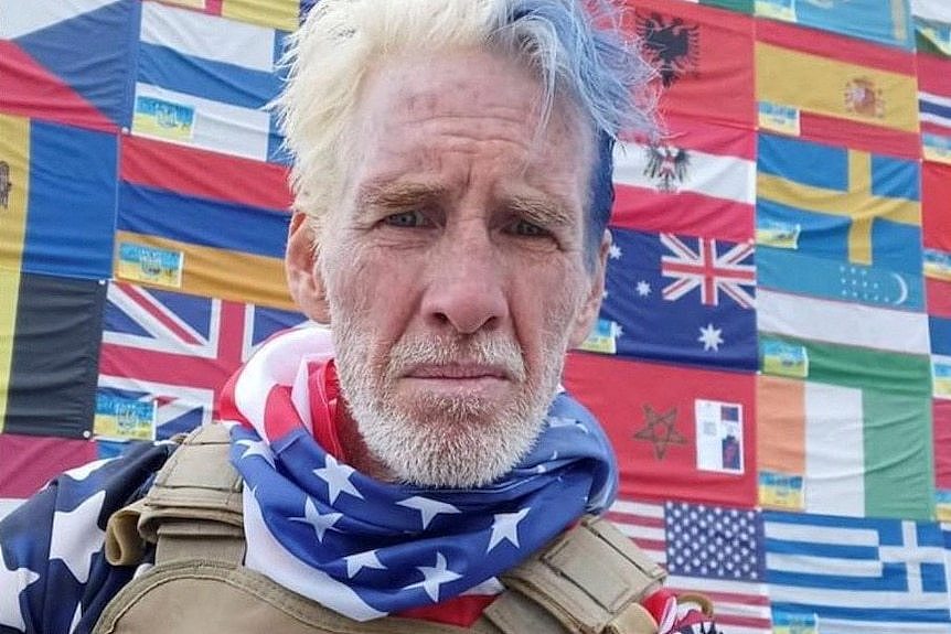 Ryan Routh pictured in a selfie with maps of the world behind him.