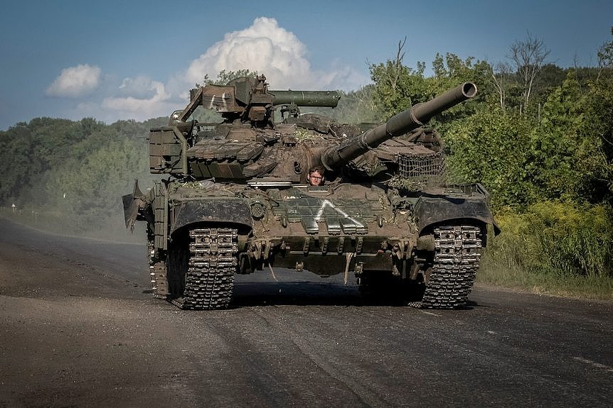 A person sits in a tank sitting on a road next to bushes.