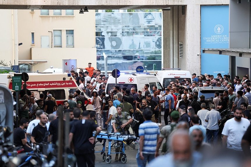 Hundreds of people gather outside a hospital between ambulances