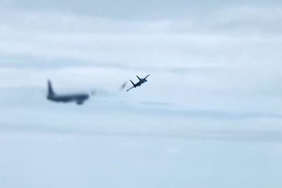 A fighter jet releasing flares in front of a larger plane.