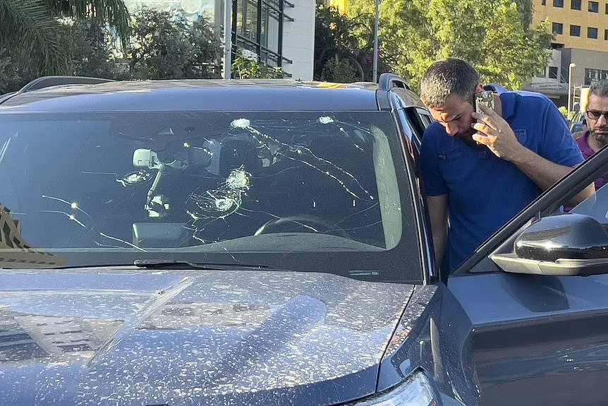 A police officer inspects a damaged car in Lebanon following pager explosions.